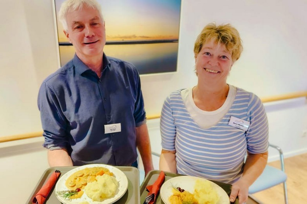 Zwei ehrenamtliche Köche halten Teller mit Speisen.