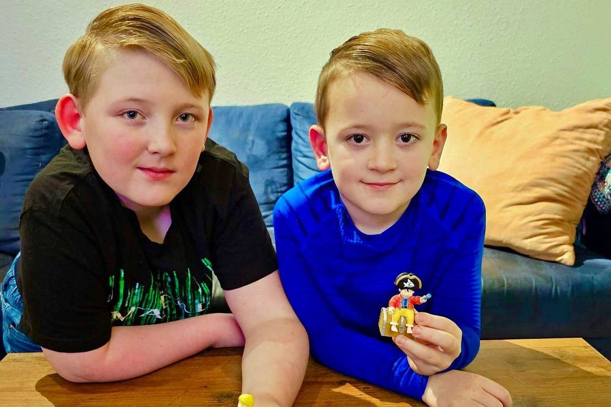 Zwei Kinder sitzen auf einer Couch mit Spielzeugen.