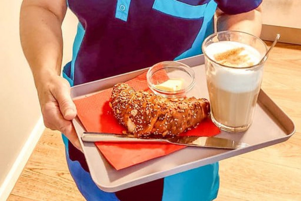 Pflegekraft trägt ein Tablett mit Frühstück.