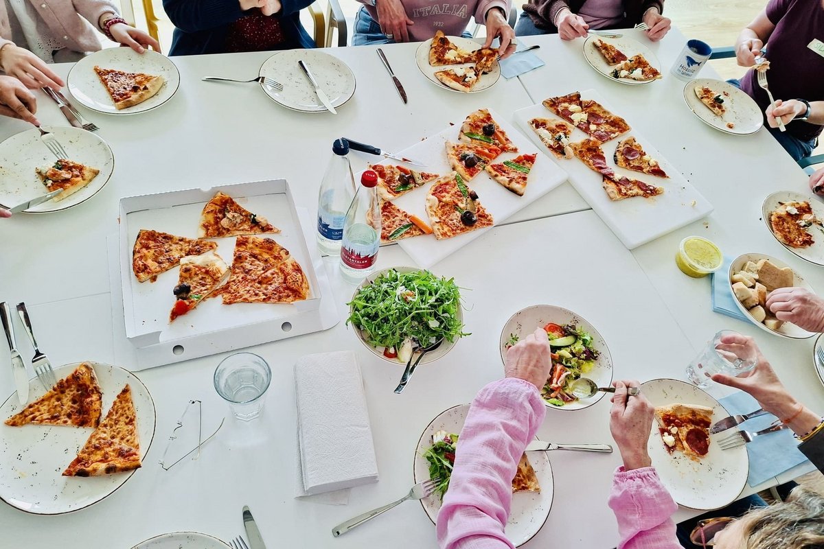 Ehrenamtler um einen Tisch herum beim Pizza und Salat essen 