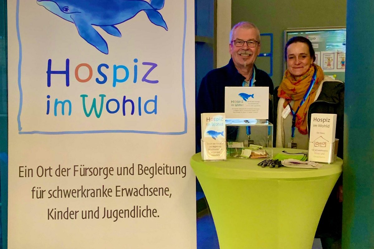 Zwei Personen stehen vor einem Schild mit der Aufschrift "Hospiz im Wohld".
